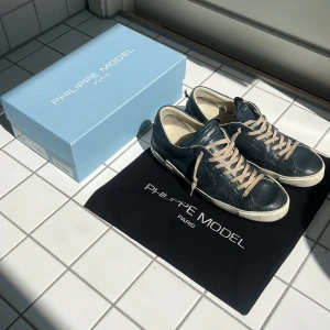 Mörkblå sneakers från Philippe Model - Säljer ett par Philippe Model sneakers i mörkblått skinn med beige snörning och vit sula. Klassisk låg modell med rund tå och diskret logga på sidan. Skorna kommer med originalkartong och dustbag. Pris kan diskuteras!