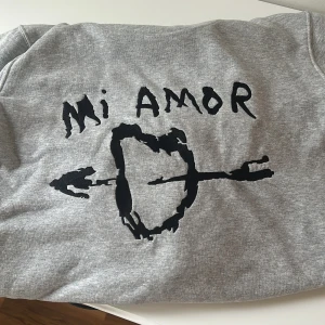 Grå hoodie Mi Amor från Mira Paris - Grå hoodie från Mira Paris med svart tryck på ryggen där det står 'Mi Amor' och ett hjärta genomborrat av en pil. Tröjan har luva med snöre, magficka och är tillverkad i mjuk ekologisk bomull. Perfekt för chill dagar och streetstyle.Säljer då den inte används.Det är storlek xxs men är nästan som S.Den är riktig jag köpte från hemsidan.