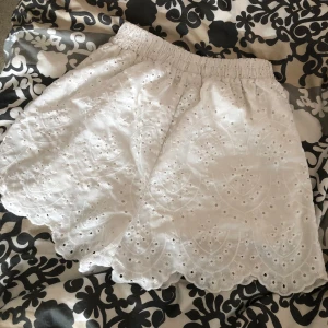 Vita tyg shorts med spetskant längs ner.  - Superfina vita shorts med blommor och spetskant. De har elastisk midja och är perfekta för varma dagar. Luftiga och lätta i bomull, med snyggt mönster och vågig nederkant som ger en söt och somrig vibe.