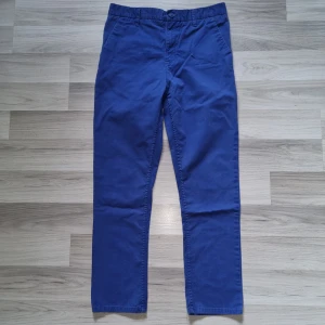 Blå chinos från H&M, stl 164 - Snygga blå chinos från H&M i storlek 164. Klassisk modell med raka ben, sidfickor och en bakficka med knapp. Byxorna har hällor för bälte och är tillverkade i mjuk bomull för en bekväm känsla.
