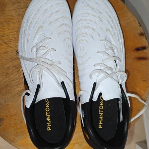 Nike Phantom GX fotbollsskor vit/svart/guld - Hej, Säljer mina fotbollsskor som används en gång bara. Nypris 1099kr men köpte för 549lr och det var rabatt.