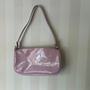Ljuslila axelväska från Gina Tricot - Säljer en ljuslila axelväska i glansigt material från Gina Tricot. 💜Väskan har dragkedja och i väskan finns ett litet fack som också stängs med dragkedja🌸Bara använd 1 gång!