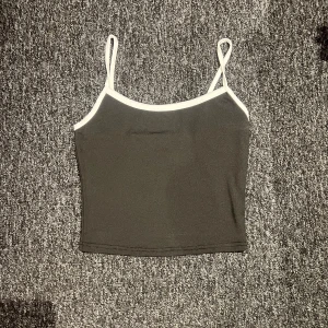 Svart croppad linnetopp med vita kanter - Säljer en svart croppad linnetopp med tunna vita axelband och vita kanter. Toppen har en enkel och stilren design, perfekt att matcha med jeans eller kjol.