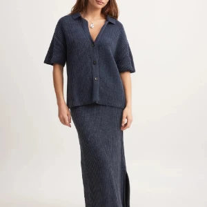 Ribbad topp - Säljer en mörkblå ribbad topp från NaKd. Den har korta ärmar, v-ringning och knappar framtill. Tillverkad i ett mjukt stickat material som ger en avslappnad men stilren look.