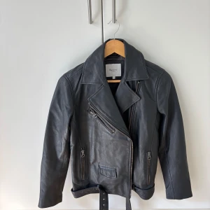 Svart skinnjacka från Pepe Jeans - Säljer en svart skinnjacka från Pepe Jeans. Jackan har bälte i midjan och flera fickor med dragkedja. Perfekt för dig som vill ha en tidlös och cool look.