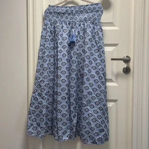 Blå långkjol med mönster från Gina Tricot - Superfin långkjol från Gina Tricot i ljusblått och mörkblått med ett unikt mönster. Kjolen har smock i midjan och dekorativa tofsar framtill. Använd fåtal gånger och i storlek 170❤️skriv om du undrar något