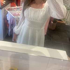 Vit kortklänning med puffärmar - Superfin vit kortklänning med transparenta puffärmar och diskret prickigt mönster. Klänningen har markerad midja, fyrkantig ringning och flowy kjol. Perfekt för sommarens alla tillfällen. Materialet känns lätt och luftigt. Har bara använt en gång och ser ut som ny 