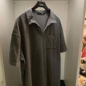 Grå frotté pikétröja  - Säljer en grå pikétröja i mjuk frotté från 157. Tröjan har korta ärmar, klassisk krage och en bröstficka. Perfekt för en chill och avslappnad stil. Aldrig använd