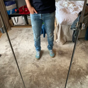 Replay Grover ljusblå jeans herr - Säljer ett par Replay Grover jeans i ljusblå tvätt med slitna detaljer och klassisk femficksdesign. Jeansen har normal passform och raka ben, tillverkade i mjuk bomullsdenim. Snyggt läderpatch bak och diskret Replay-logga på fickan.