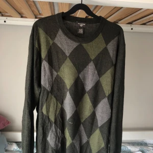 Grön rutig tröja från Dockers XL - Snygg stickad tröja från Dockers i storlek XL. Tröjan är mörkgrön med rutigt mönster i grönt och grått framtill. Rund halsringning och långa ärmar. Liten i storleken, den passar mig som tjej med storlek M (lite oversized).
