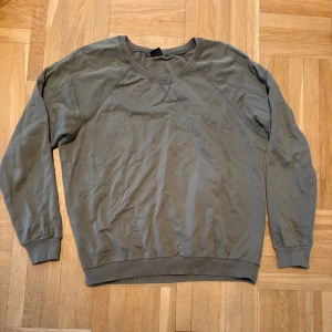 Olivgrön sweatshirt från Gina Tricot - En basic olivgrön sweatshirt från Gina Tricot i storlek M. Tröjan har rund halsringning, ribbade muddar vid ärmslut och nederkant samt långa ärmar. Perfekt för en avslappnad och stilren look.