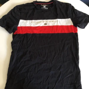 Christian Berg t-shirt med ränder - Snygg t-shirt från Christian Berg i svart med breda horisontella ränder i vitt och rött över bröstet. Tillverkad i mjuk Supima-bomull som känns riktigt skön mot huden. Klassisk passform och korta ärmar, perfekt för en stilren look.