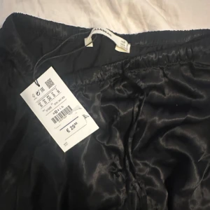 Svarta vida byxor från Pull&Bear - Säljer ett par svarta, glansiga byxor från Pull&Bear . Aldrig använda me prislapp kvar