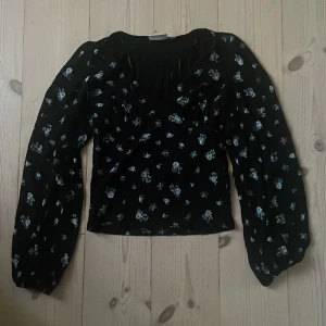 Svart blommig blus från Kappahl - svart blus från Kappahl med små blå och vita blommor. Blusen har v-ringning, långa ärmar och en lätt figurnära och bra passform. 
