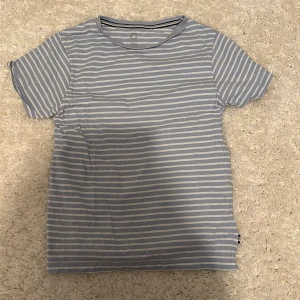 Blåvit randig t-shirt från Cubus - Snygg blå och vit randig t-shirt från Cubus i mjuk bomull. Klassisk rund halsringning och korta ärmar. Perfekt för en chill och avslappnad stil. Passar dig som gillar enkel och fräsch design. Barn storlek 146\152