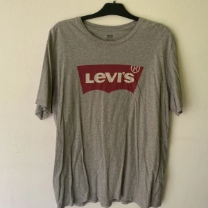 Grå Levi's t-shirt med röd logga - Snygg grå t-shirt från Levi's med klassisk röd logga framtill. T-shirten har rund halsringning och korta ärmar. Tillverkad i mjuk bomull som är skön att ha på sig. Perfekt för en avslappnad och stilren look.