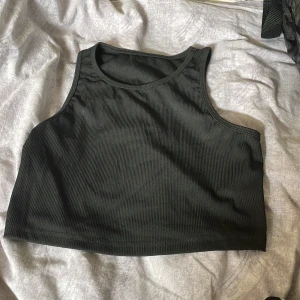 Svart ribbad croppad linnetopp - Säljer en svart croppad linnetopp med ribbad struktur. Toppen är ärmlös och har en rund halsringning, perfekt för en clean och sportig look. Enkel att matcha med både jeans och kjol.
