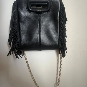 Svart axelväska med fransar från Maje - den minsta majeväskan i svart. texten vid handtaget har försvunnit lite grann men annars är väskan i jätte fint skick, skriv för fler bilder. både kedjan och den andra skinnremmen + dustbag följer med. pris kan diskuteras!