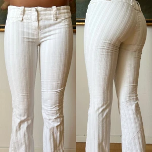 Vita randiga bootcut byxor - Snygga vita byxor med diskreta vertikala ränder och bootcut-snitt. Byxorna har breda hällor, dragkedja och knapp framtill. De sitter tajt över låren och släpper ut vid bensluten för en trendig siluett. Perfekta för dig som gillar stilrena och fräscha vibes.