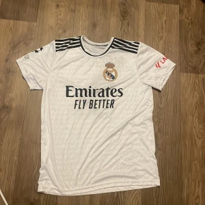 Real Madrid Mbappé 9 matchtröja - Snygg vit Real Madrid fotbollströja med Mbappé och nummer 9 på ryggen. Adidas-logga, svarta ränder på axlarna och klubbmärke på bröstet. Tryck från La Liga och UEFA Foundation på ärmarna. Tillverkad i lätt och ventilerande material, perfekt för fotbollsplanen.