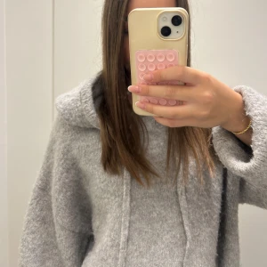 Grå stickad hoodie från Gina Tricot - Supermjuk och oversized grå stickad hoodie från Gina Tricot. Har stor huva och snörning framtill, perfekt för mysiga dagar. Den fluffiga känslan gör den extra cozy och den neutrala färgen passar till allt. Säljer då jag rensar garderoben!