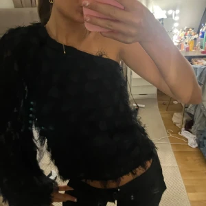 Svart oneshoulder topp med fluffig struktur - Säljer en svart oneshoulder topp med lång ärm och cool fluffig struktur. Toppen har en unik look med prickig textur och är perfekt för dig som vill sticka ut. Sitter snyggt och ger en edgy vibe till outfiten.