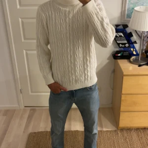 Vit stickad polotröja TREpuntoNOVE - Säljer en vit stickad polotröja från TREpuntoNOVE. Tröjan har klassiskt kabelstickat mönster, hög polokrage och långa ärmar. Perfekt för lager-på-lager och chill höst- eller vinterstil. Snygg till både jeans och dressade byxor.