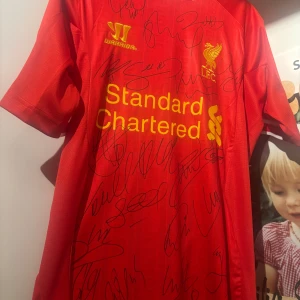 Liverpool signerad matchtröja Warrior M - Röd Liverpool fotbollströja från Warrior i storlek M, tillverkad i 100% polyester. Tröjan har korta ärmar, klubbmärke och sponsortryck i gult samt flera autografer från spelare. Levereras med äkthetsintyg från Harrison Autographs.Varan är i jättebra skick inga defekter utan bara autografer med spelare som, Steven Gerrard, Jordan hendersson, raheem sterling och luis suarez. Kom privat för fler bilder på lappar och liknande