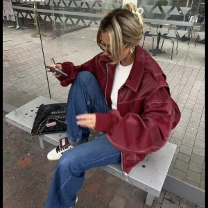 Röd oversized skinnjacka med dragkedja - Säljer en riktigt snygg röd skinnjacka i oversized modell med markerade sömmar och dragkedja framtill. Jackan har bred krage, långa ärmar och coola detaljer som ger en trendig vibe. Perfekt att slänga över en hoodie eller t-shirt för en chill streetstyle-look.