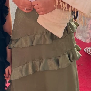 Olivgrön långklänning med volanger - En välbehållen klänning som bara är använd 1 gång. Skönt material och fin färg! Klänningen har snygga volanger. Sitter ner till anklarna på en tjej som är 172 cm. Går att diskutera pris!