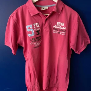 Rosa pikétröja från 8848 Altitude - Snygg rosa pikétröja från 8848 Altitude med broderade och tryckta detaljer framtill. Klassisk krage och korta ärmar, perfekt för en sportig och avslappnad look. Tillverkad i mjuk bomull som känns skön mot huden.