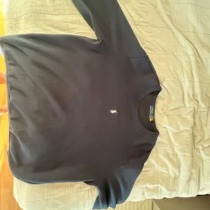 Mörkblå crewneck från Polo Ralph Lauren - Säljer en stilren mörkblå crewneck från Polo Ralph Lauren med klassisk vit broderad logga på bröstet. Tröjan har rund halsringning, långa ärmar och ribbade muddar. Perfekt för dig som gillar enkel och tidlös stil.