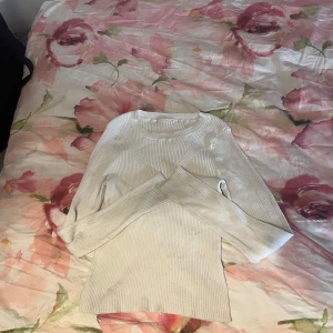 Ljusbeige ribbad stickad tröja - Supersnygg ljusbeige stickad tröja med ribbad struktur. Tröjan har lång ärm och en klassisk rund halsringning. Perfekt att matcha med jeans eller kjol för en clean och stilren look.