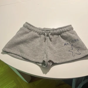 Grå mjuka shorts med snörning low waist - Superbekväma lågmidjade grå shorts i mjuk bomull med elastisk midja och snörning. På vänster sida finns en blå stjärna och texten 'MA CHERIE' tryckt. Perfekta för chill dagar eller när du vill ha något enkelt och snyggt. Pris kan diskuteras
