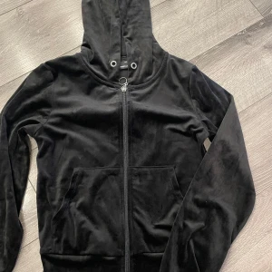 Svart velour hoodie från Gina  - Svart hoodie i mjuk velour från Marboo med dragkedja framtill och huva. Jackan har långa ärmar och praktiska fickor på magen. Perfekt för en chill och avslappnad stil.