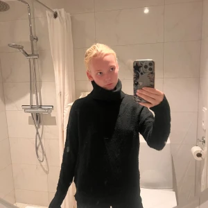 Svart polotröja i stickat material - Mysig svart polotröja i stickat material med hög krage och långa ärmar. Tröjan har en loose passform och är perfekt för kyliga dagar. Enkel och stilren design som funkar till många olika outfits.