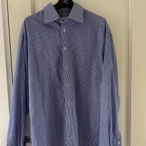 Blåvit randig skjorta med knappar från Eton - Klassisk blå skjorta med tunna vita ränder och knäppning framtill. Skjortan har lång ärm, bred krage och är tillverkad i ett mjukt bomullstyg. Perfekt för en clean och stilren look.