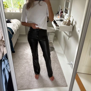 Svarta raka byxor i skinnimitation - Säljer ett par svarta byxor i skinnimitation från Bik Bok. De har raka ben, hög midja och klassiska fickor både fram och bak. Snygg passform och stilren look som passar till allt. Stängs med dragkedja och knapp framtill. Prislappen är kvar! 