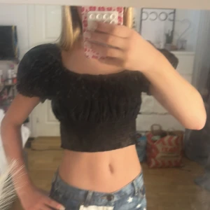 Svart croppad blus med puffärmar - Supersöt svart croppad blus med puffiga korta ärmar. Toppen har broderade hål och en liten knytning framtill. Det går också att ha den offshoulder om man vill. Säljer den eftersom den inte kommer till användning längre. Kontakta gärna innan köp. OBS, katt finns i hemmet!