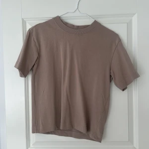 Beige basic t-shirt från Gina Tricot - En stilren beige t-shirt från Gina Tricot, basically basics-kollektionen. T-shirten har rund hals, korta ärmar och är gjord i mjuk bomull. Perfekt till jeans eller kjol för en clean och enkel look. Säljer då den inte kommer till användning. Knappast använd och som i nyskick. Storleken är xxs. 