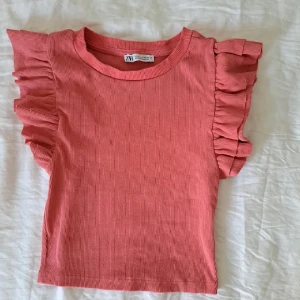 Rosa ribbad topp med volangärmar Zara - Supersöt rosa topp från Zara med ribbad struktur och volangdetaljer på axlarna. Modellen är croppad och har en rund halsringning. Perfekt för dig som gillar en lekfull och trendig stil.