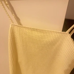 Ribbad ljusbeige linnetopp - Säljer en ribbad ljusbeige linnetopp med smala axelband. Toppen har en enkel och clean look, perfekt att styla med jeans eller kjol. Materialet är mjukt och följsamt, vilket gör den superbekväm att bära.