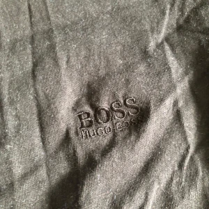 Svart t-shirt från Hugo Boss - Snygg svart t-shirt från Hugo Boss med broderad logga på bröstet. Klassisk rund halsringning och korta ärmar. Tillverkad i mjuk bomull som känns skön mot huden. Perfekt för en clean och stilren look.