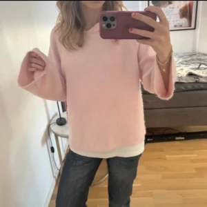 Ljusrosa stickad hoodie med vida ärmar - Supermysig ljusrosa stickad hoodie med vida ärmar och avslappnad passform som har ett igen sytt hål. Tröjan har en luva och är perfekt för dig som gillar en chill och söt stil. Passar extra bra till höst och vinter när du vill vara varm och comfy.