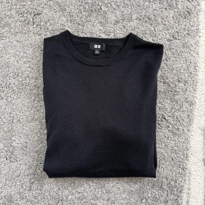 Svart merino tröja från Uniqlo - En klassisk svart stickad tröja från Uniqlo med rund halsringning. Perfekt basic-plagg som funkar till allt och är lätt att matcha. Tröjan har en enkel och stilren design med mjukt material som känns skönt mot huden.