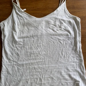 Vit linnetopp från 157, storlek S - Enkel och stilren vit linnetopp från 157 med smala axelband och mjuk känsla. Toppen är tillverkad i bomull med lite stretch för extra komfort. Perfekt att matcha med jeans eller kjol för en clean look.
