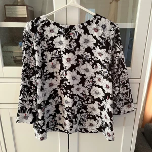 Blommig blus från Esprit - Säljer en svartvit blus från Esprit som har stora vita blommor med detaljer i rött och blått. Blusen har trekvartsärmar och en lös passform💕