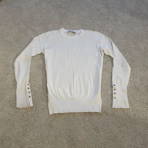 Långärmad topp - Vit långärmad tröja från Zara i mjuk och stretchig bomullsblandning. Tröjan har rund halsringning och snygga guldfärgade knappar vid ärmsluten som extra detalj. Tycker inte att den sitter bra på mig och kommer därför inte att skicka bilder när jag har den på mig💓💓