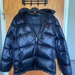 Mörkblå pufferjacka Polo Ralph Lauren - Säljer nu min vinter jacka från ralph lauren som är  i väldigt fint skick och sparsamt använd, det ända defekta är att hängaren har gått sönder. Priset är ej hugget i sten!