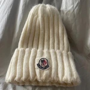 Vit ribbstickad mössa från Moncler - Använd. Har fläckar men går säkert bort i tvätten. S-M. KAN JÄTTEGÄRNA GÅ NER I PRISET.